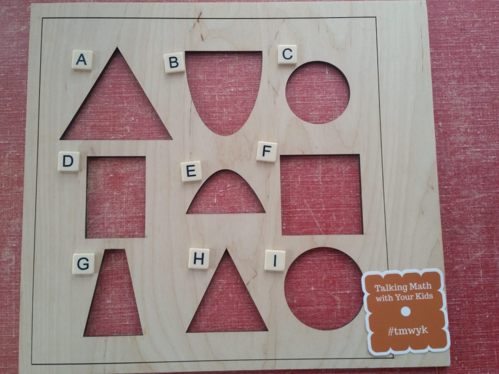 Wooden frame with cutouts labeled by letters. A: equilateral triangle, B: half ellipse, C: small circle, D: rectangle (taller than it is wide), E: parabola, F: square, G: tall skinny isosceles trapezoid, H: isosceles triangle, I: large circle