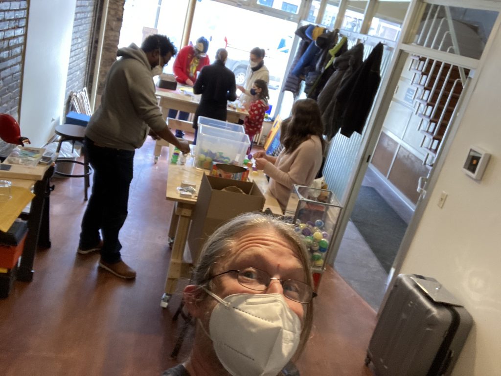 A selfie of the author, with several adults and children in the background packing vending machine capsules on a sunny winter day.