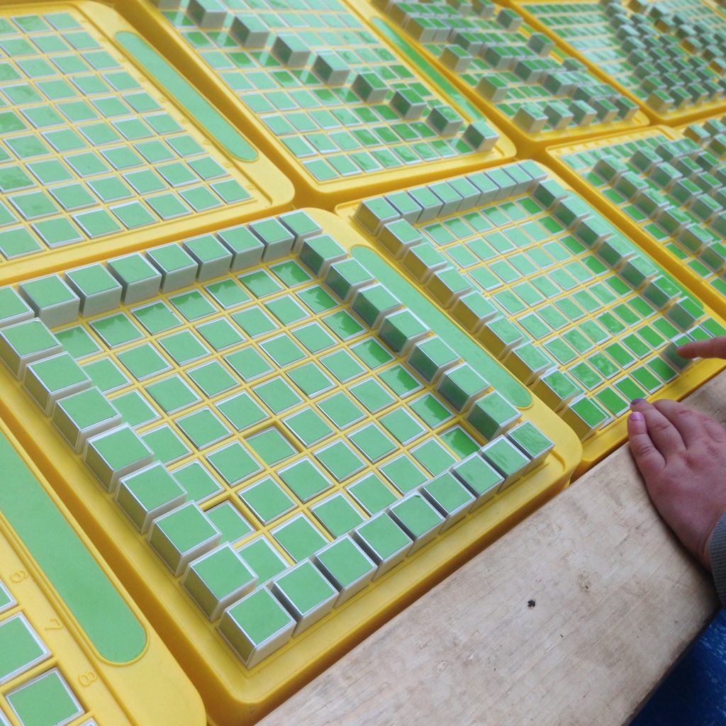 A close up of the mega pattern machine—a child's hand makes a square on one of the approx. 8 machines in view.