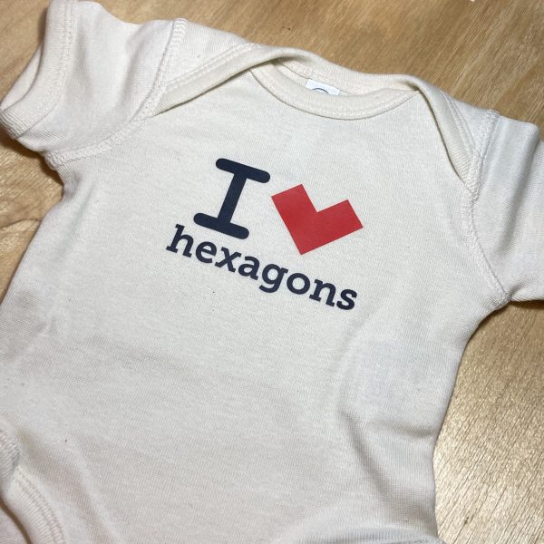 An off-white baby bodysuit that reads "I *heart* hexagons" but where the heart is actually a red, concave hexagon standing on a vertex.