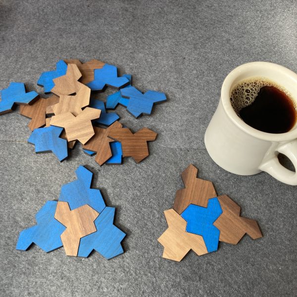 A cup of coffee inspires the mathematician who has made two small subtilings of hat tiles—each a triangle of sorts with three blue tiles surrounding a brown, or vice versa.