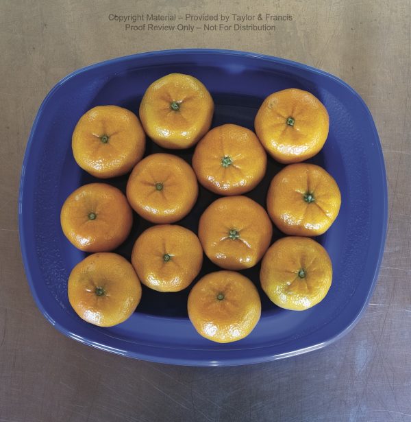 A blue, oblong bowl rests on a wooden surface. The bowl contains an arrangement of tangerines—four columns of three tangerines each, in an offset, isometric pattern.